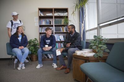 Three students laughing while chatting with a staff member of the Student Life Office