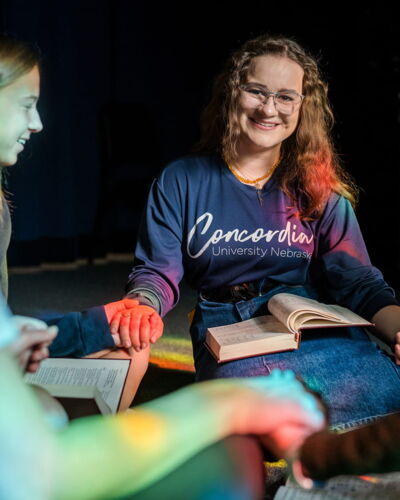 Students holding hands in a circle with Bibles open in their laps