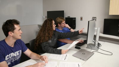 Three computer science students looking at a computer monitor during a programming competition. 
