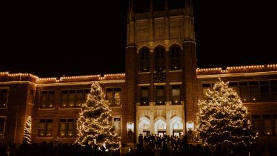 the pine trees in front of Weller Hall lit up with Christmas lights as students sing Christmas carols
