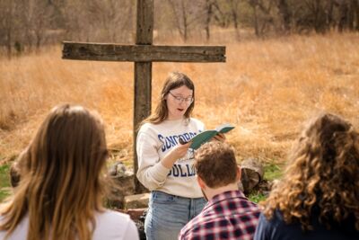 A. student reading to other students from the Bible at the outdoor chapel