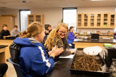 Two students participating in an ag science lab demonstration with one smiling as the other holds some eggs. 