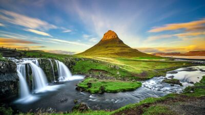 Icelandic landscape featuring a cascading waterfall surrounded by green grass and rugged mountain terrain.