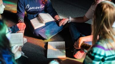 Students sitting in a circle, holding hands with hymnals open in front of them
