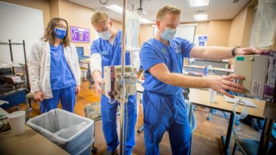 Three nurses set up medical equipment in a hospital room
