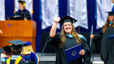 A graduate student waves with her diploma at commencement.