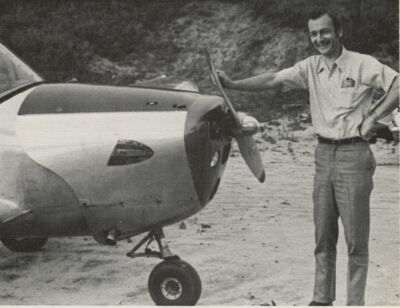 Charles Krutz smiling next to a small airplane while resting his hand on the propeller.