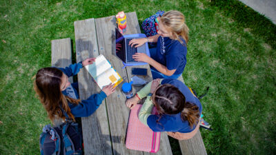 An aerial shot of three students studying textbooks at a picnic table