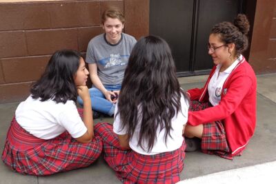 A Concordia student on a mission trip in Guatemala, sitting on the ground with three local students. 