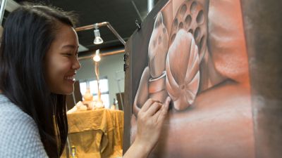 A female Concordia student adds finishing touches to her drawing of pink flowers.