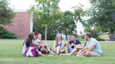 a group of Concordia students sit in the grass and visit in the quad