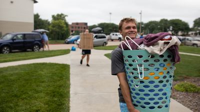 A new Concordia student carries a hamper to his dorm room during move in.