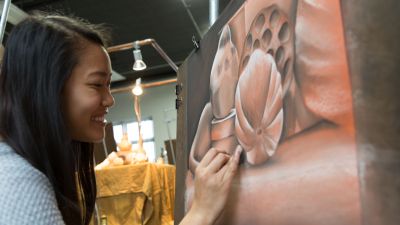 A female Concordia student adds finishing touches to her drawing of pink flowers.