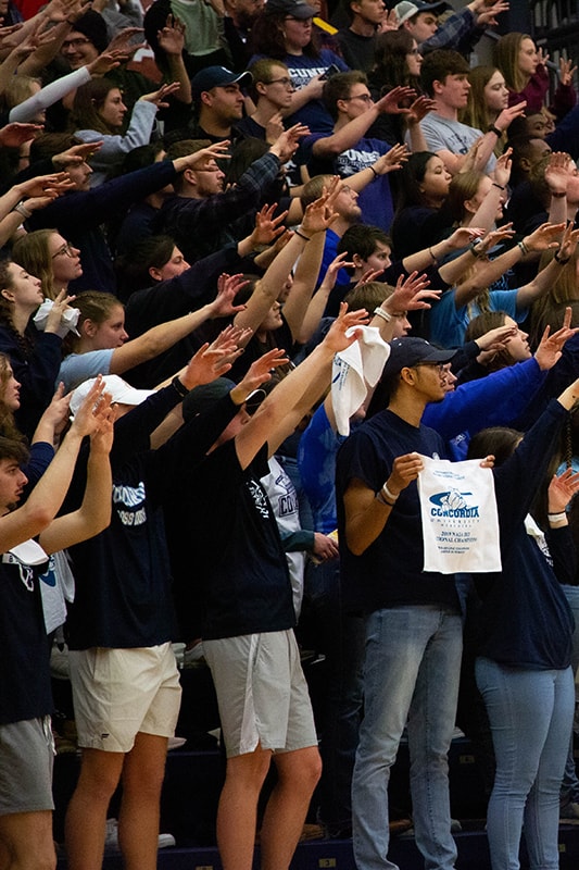 Students with arms raised, cheering on Concordia at Friedrich Arena